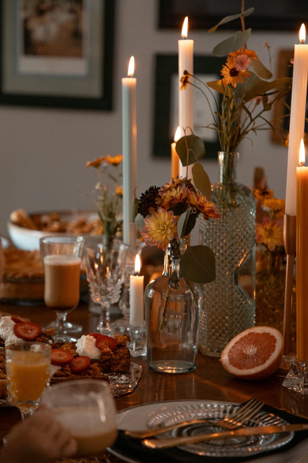 Een lange tafel bij het licht van hoge kaarsen, met glazen en gedroogde bloemen