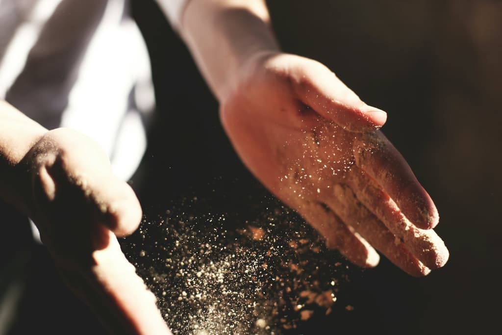 De handen van een kok strooien bloem door een bundel warm licht in een donkere keuken