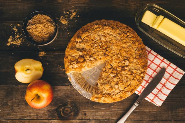 Een appelkruimeltaart naast appels en een geruite doek