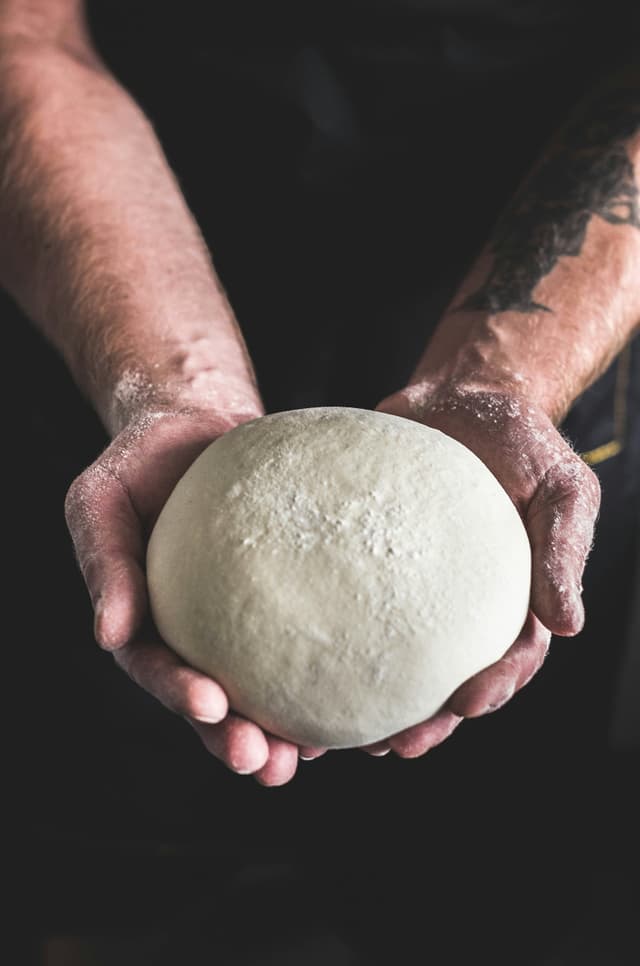 Handen vol bloem met een bal pizzadeeg